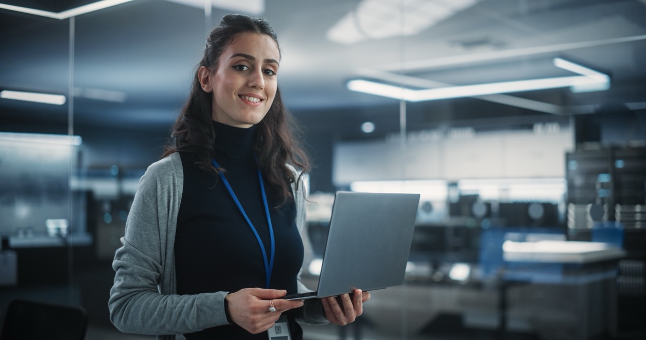 Woman holding laptop in computer lab, smiling