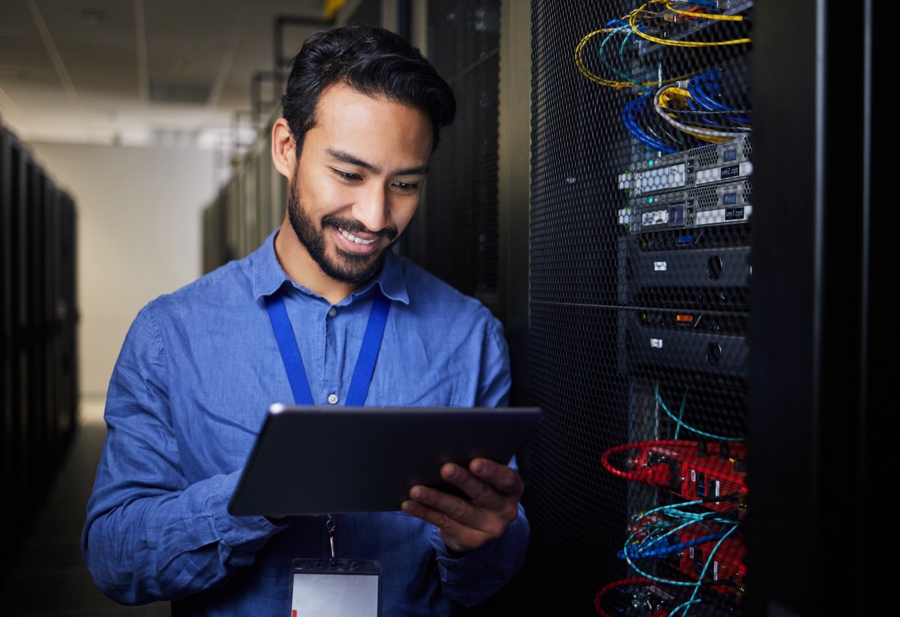 Man wearing blue collared shirt and holding tablet, working on computer system