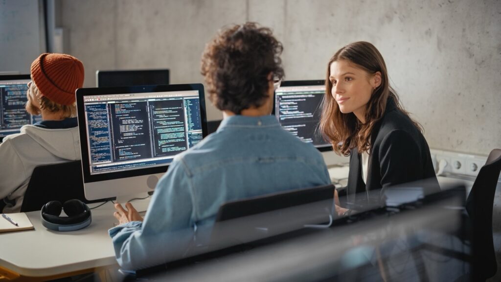 Young woman talking with man in class. Monitors open with data displayed