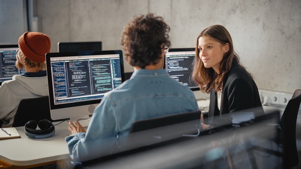 Young woman talking with man in class. Monitors open with data displayed