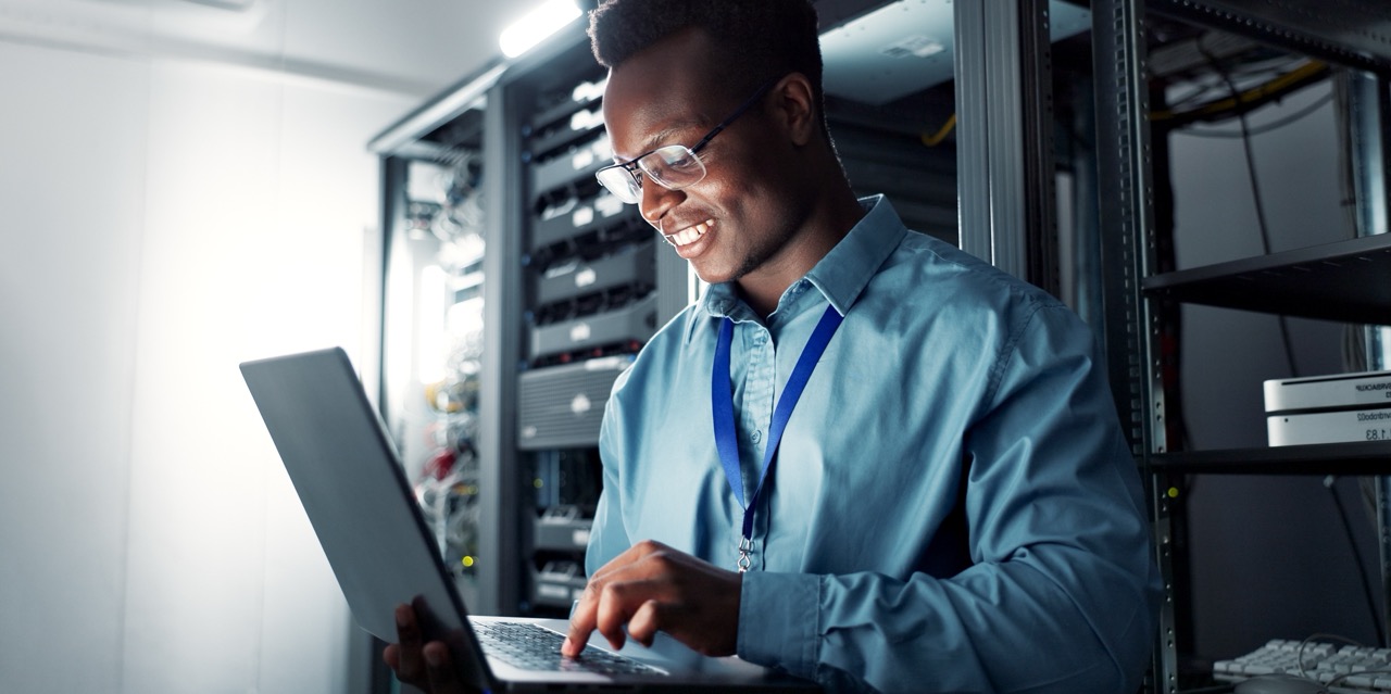 Man typing on computer, smiling wearing collared shirt and lanyard