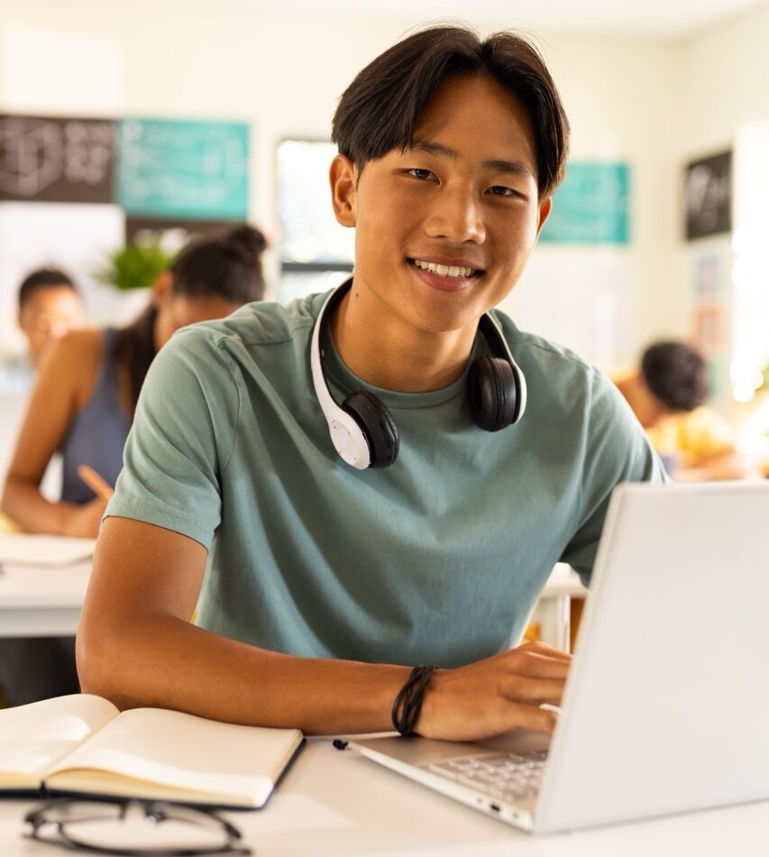Young man sitting in front of laptop with headphones around neck